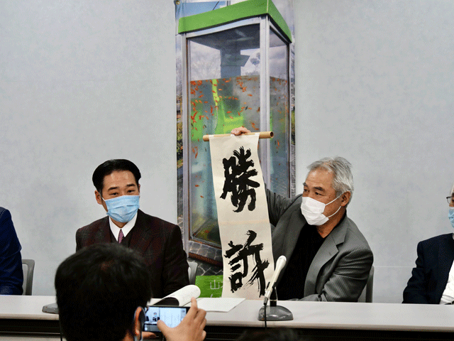 大阪高裁で「勝訴」の「びろーん」を掲げる山本伸樹